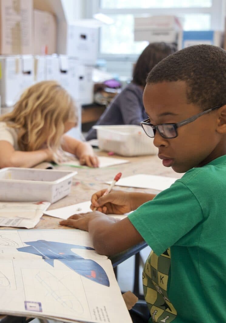 boy in green sweater writing on white paper