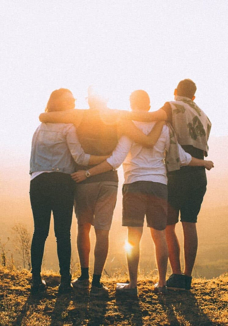 four person hands wrap around shoulders while looking at sunset